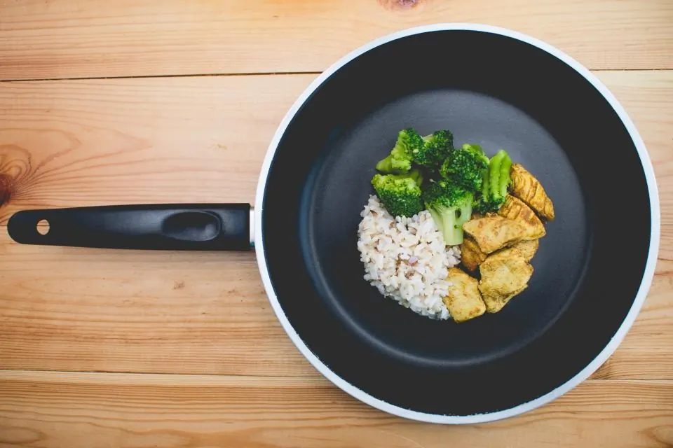 Sartén con arroz integral, brócoli y pollo sobre una mesa de madera