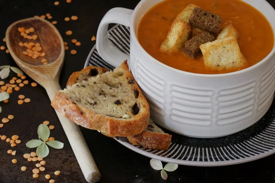 Taza de crema de lentejas rojas con picatostes y pan al lado