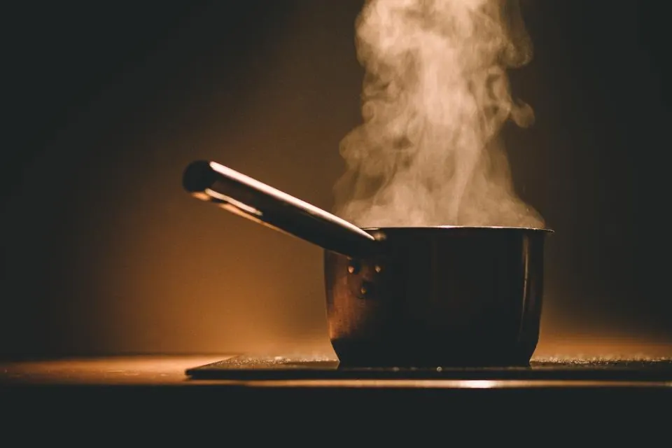 Cazo de acero humeando sobre el fuego en una cocina en penumbra