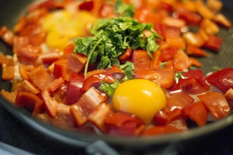 Sartén con pimientos rojos troceados, cilantro y un huevo cuajándose