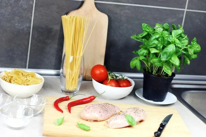 Encimera con pasta, tomates, albahaca y pollo listos para cocinar